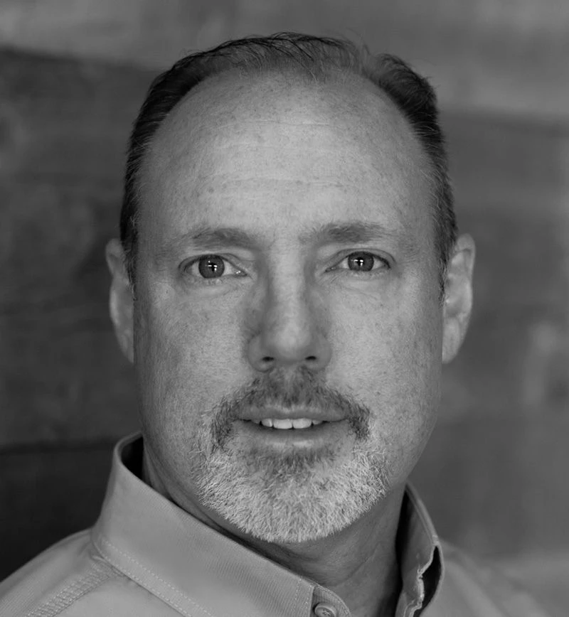 Black-and-white close-up portrait of a middle-aged man with short graying hair and a goatee, wearing a collared shirt